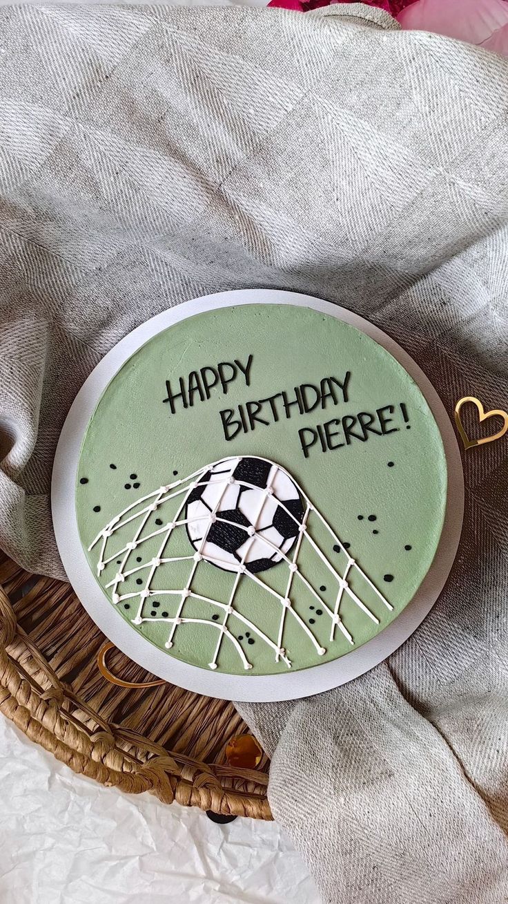 Round green card with soccer ball and net design, featuring 'Happy Birthday Pierre!' text, on a textured fabric background.